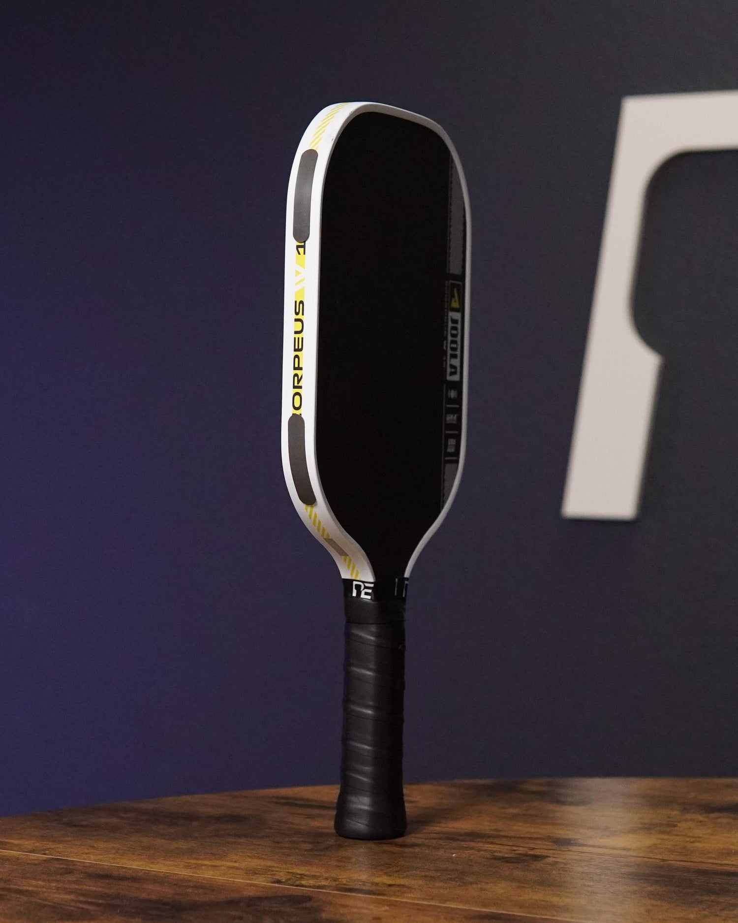 Pickleball paddle on a wooden surface with a dark background featuring a logo.